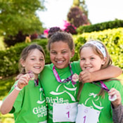 3 girls in green shirts smile while holding medals after the Girls on the Run 5K